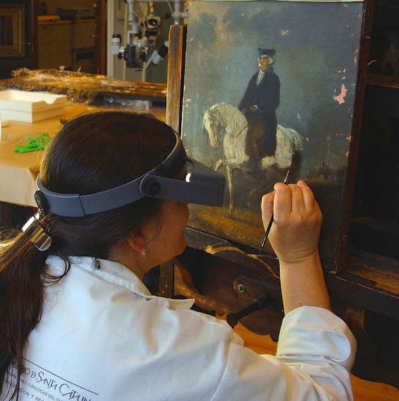 Catalina Vasquez-Kennedy inpainting an equestrian portrait at the easel, wearing a magnifying visor