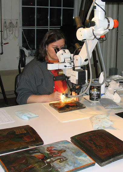 Catalina Vasquez-Kennedy examining a painted panel under a stereo microscope at the studio bench